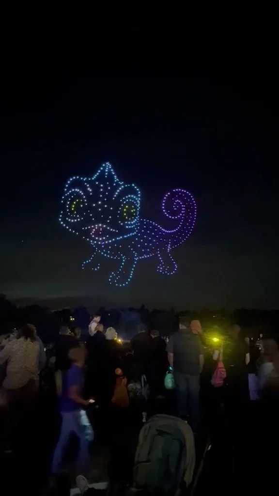 A chameleon drawn in blue and purple drone lights above a crowd at Dunorlan Park at night